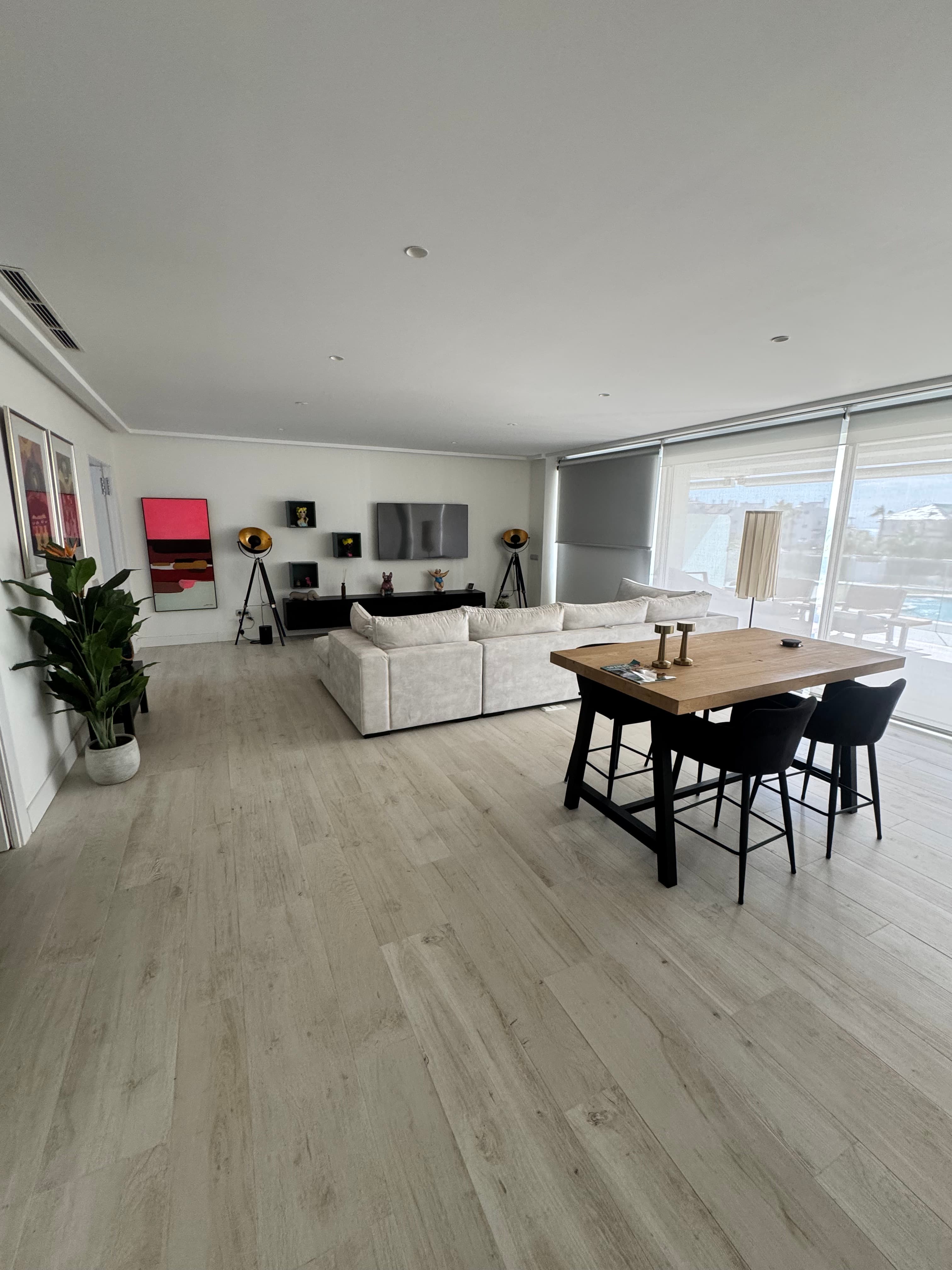 Bright modern living room with white sectional sofa, wooden dining table, and large windows.