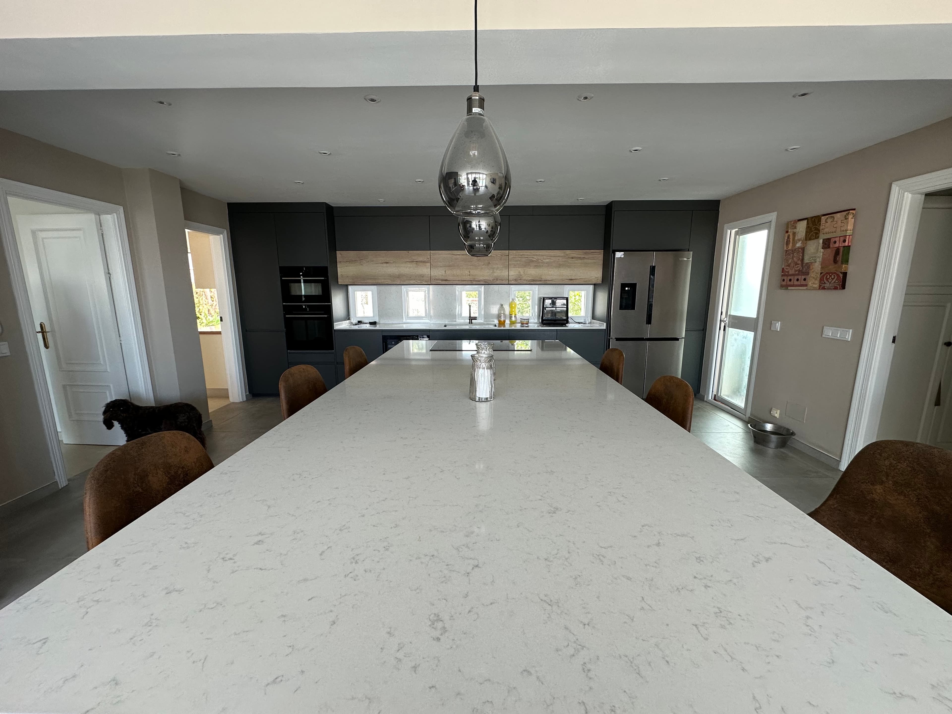 Modern kitchen with a large white marble island, dark grey cabinetry, and silver pendant light.